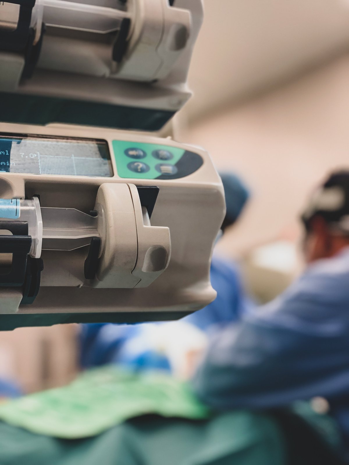 Medical drug infusion pumps in the foreground with surgeons operating in the background in operating theatre