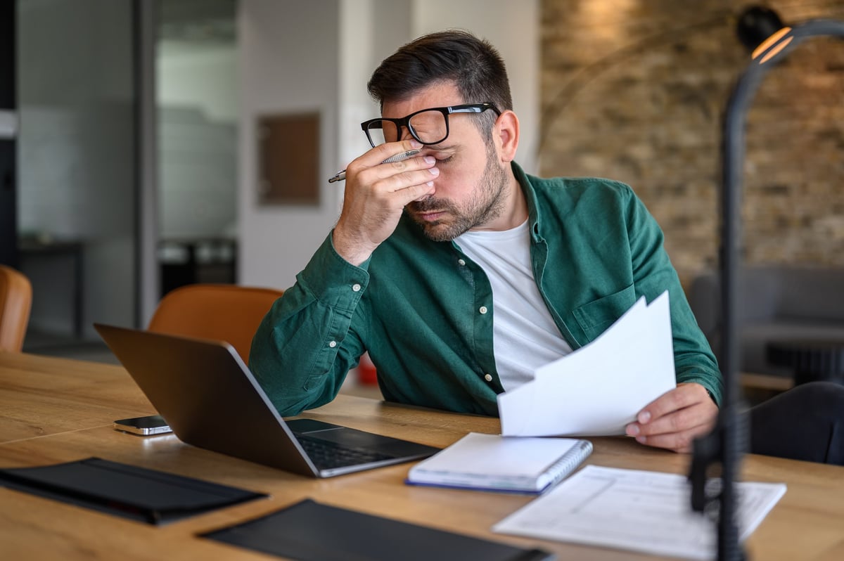 Anxious male professional rubbing eyes while working over laptop and analyzing reports at desk