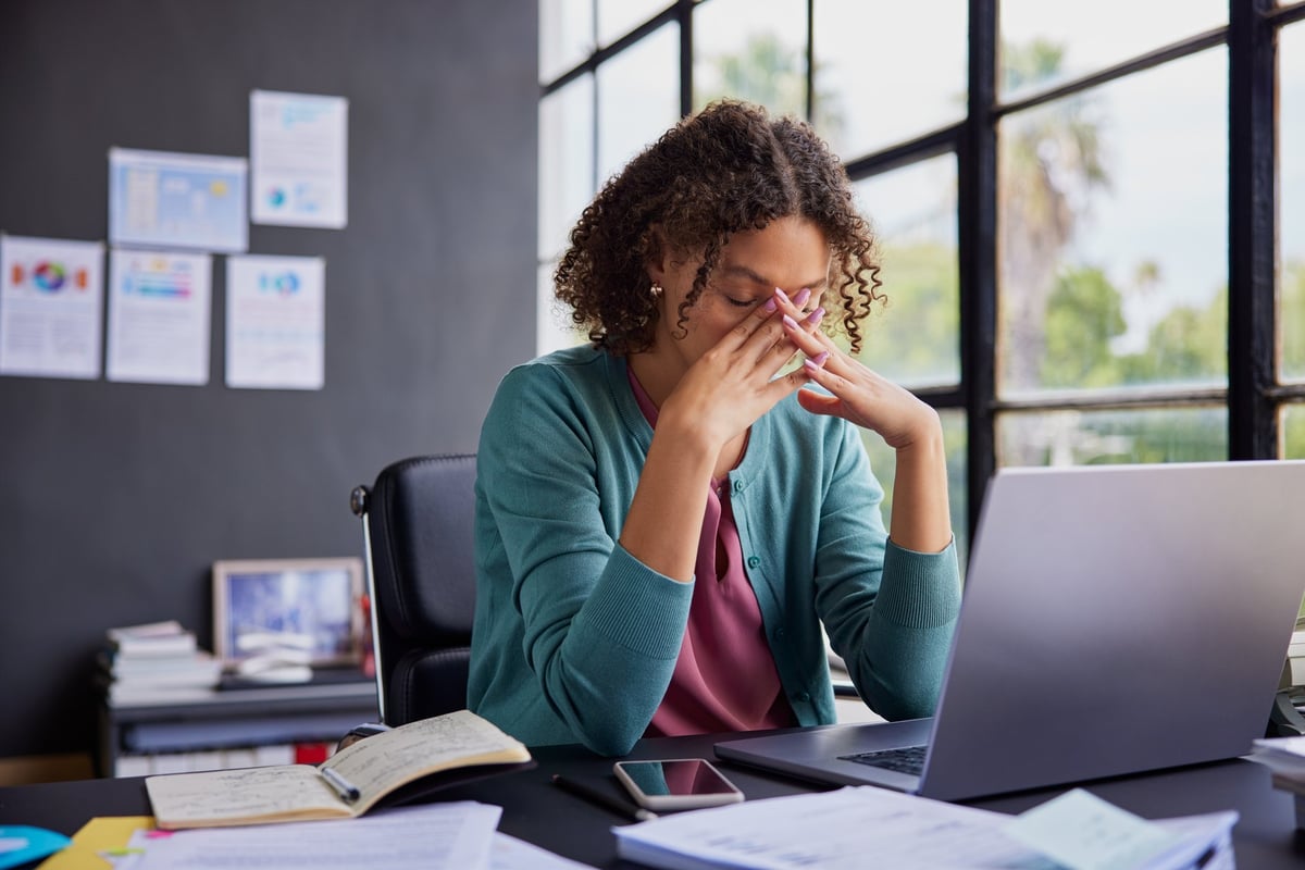 Exhausted businesswoman feeling stressed and holding her head while working on a laptop with migraine