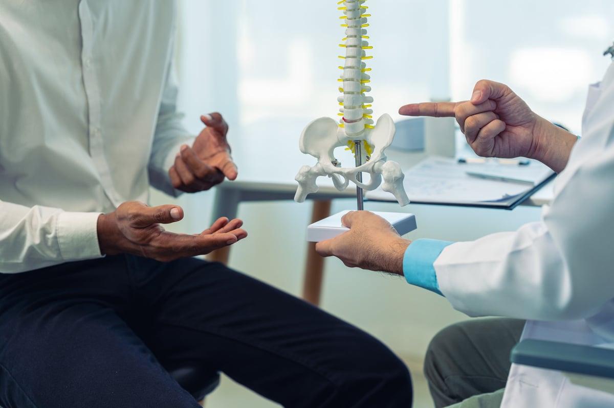 Spine model and male patient asking for advice on treatment, physical therapy, doctor explaining causes of back pain