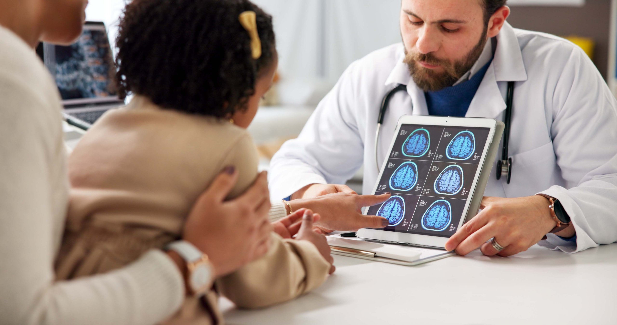 Doctor mostrando resonancia cerebral a niña y padre en consulta pediátrica neurológica