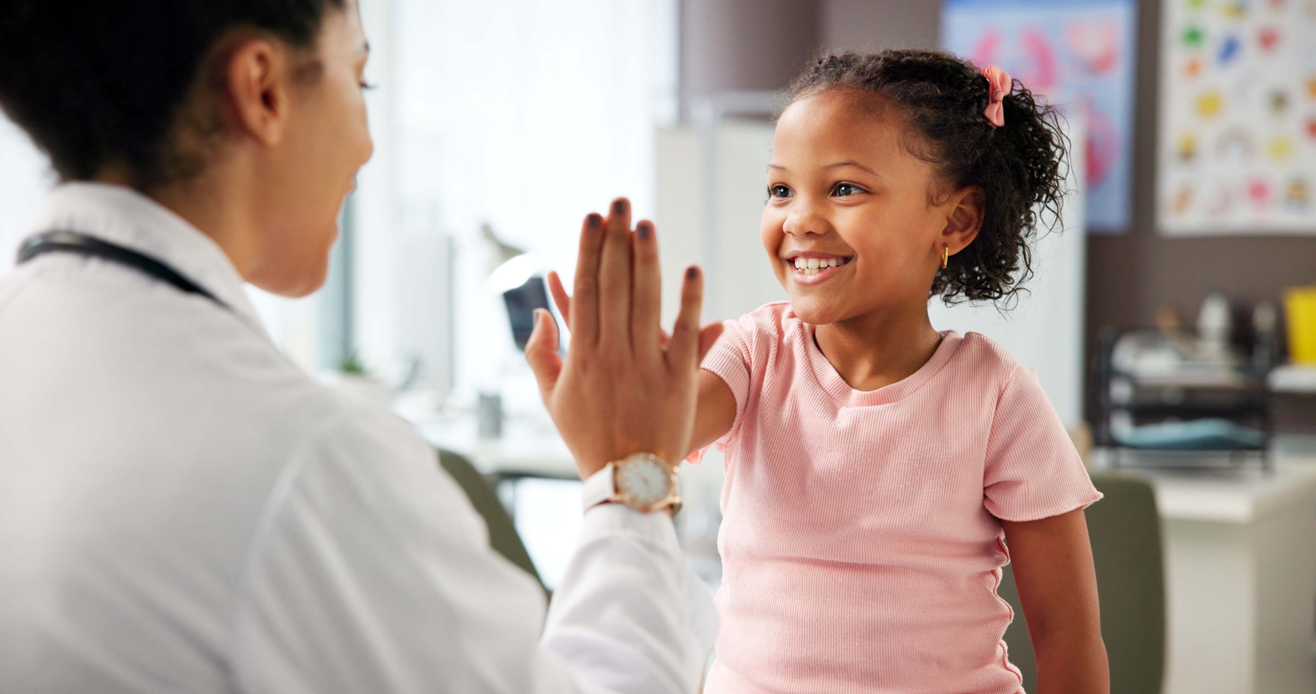Médico pediatra chocando los cinco con niña durante consulta, celebrando valentía en atención pediátrica