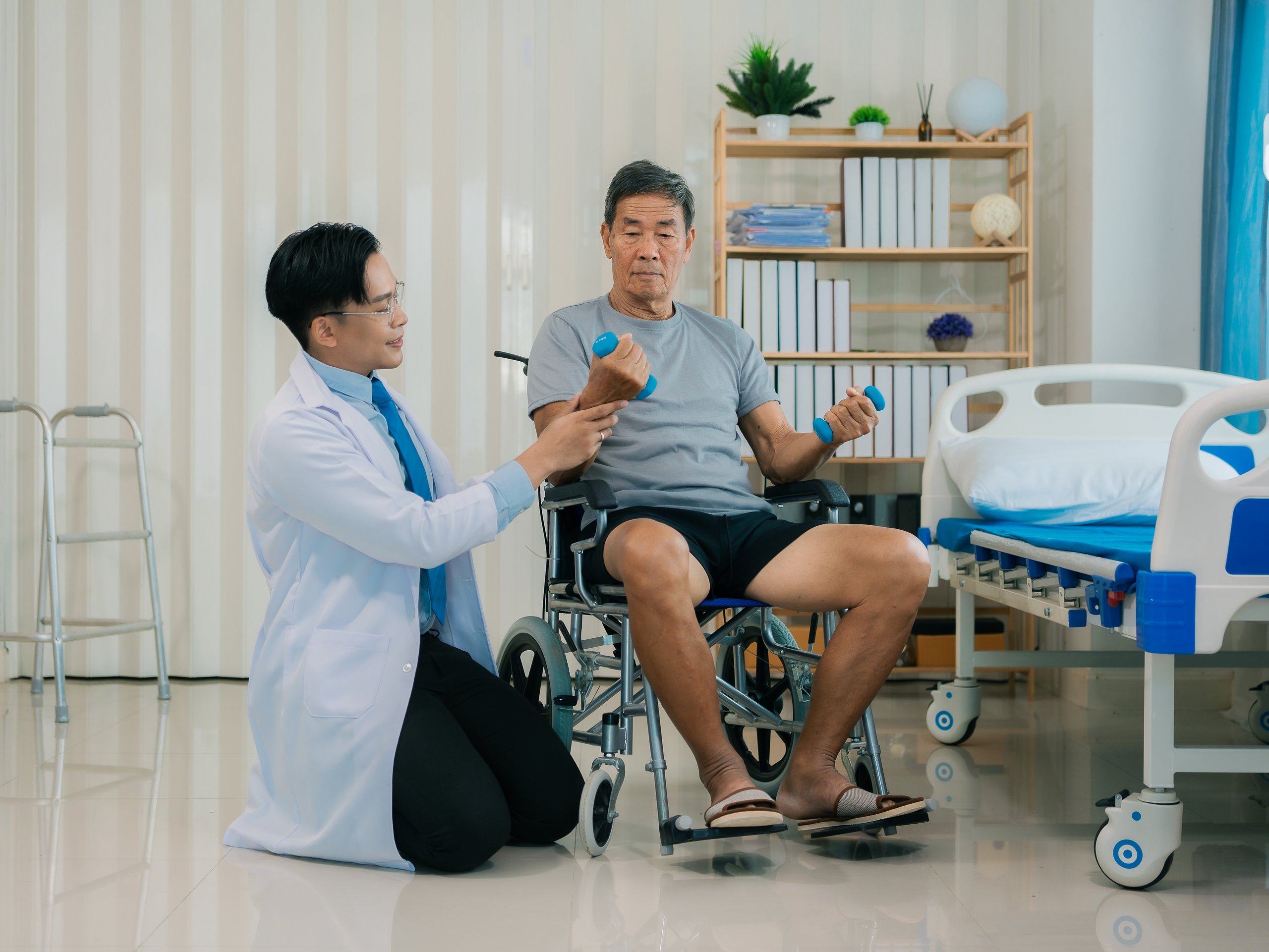 Médico asiático recomendando ejercicios de rehabilitación a paciente en silla de ruedas durante terapia
