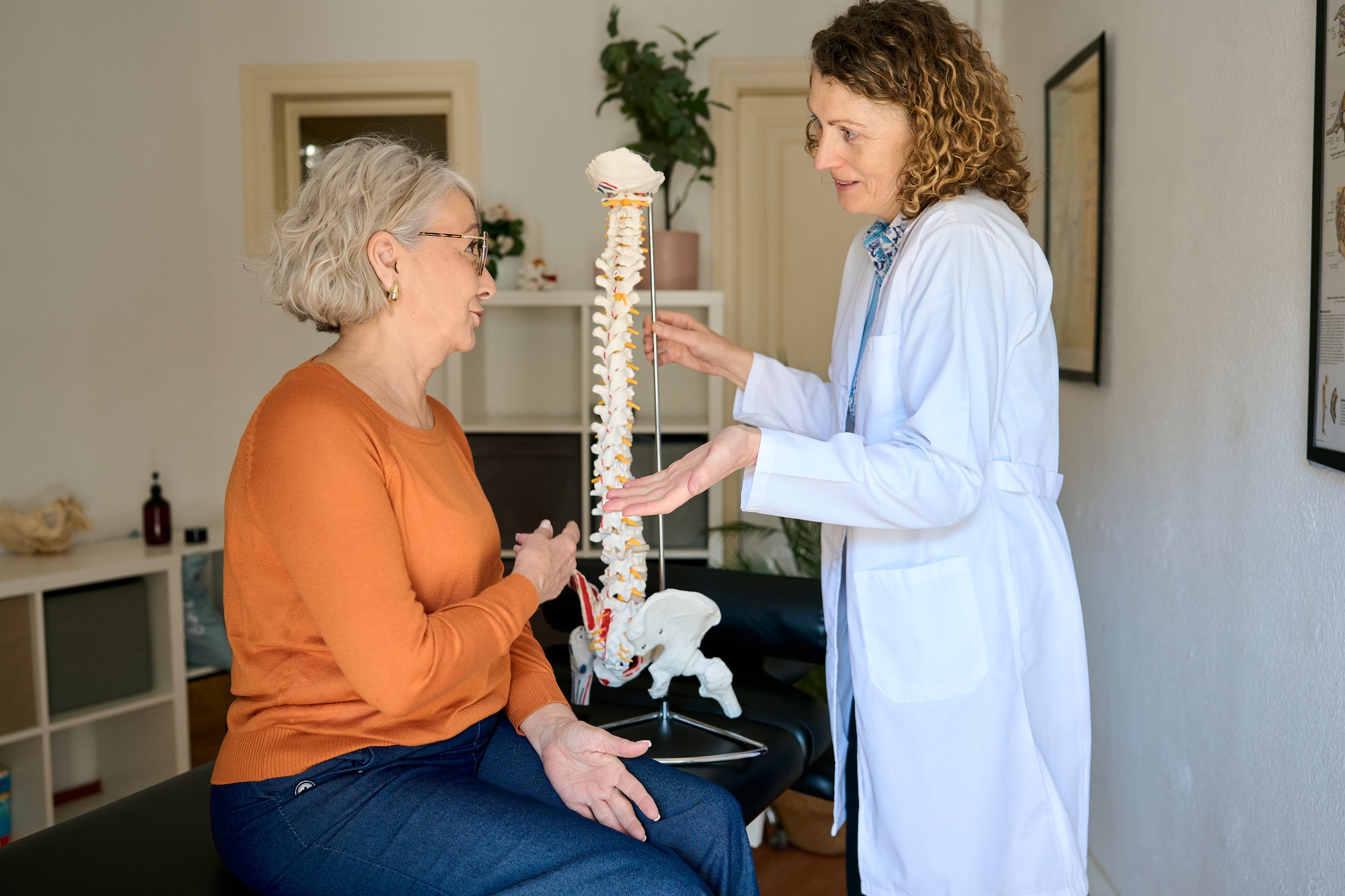 Médico mostrando modelo de columna vertebral a paciente en consulta por dolor lumbar