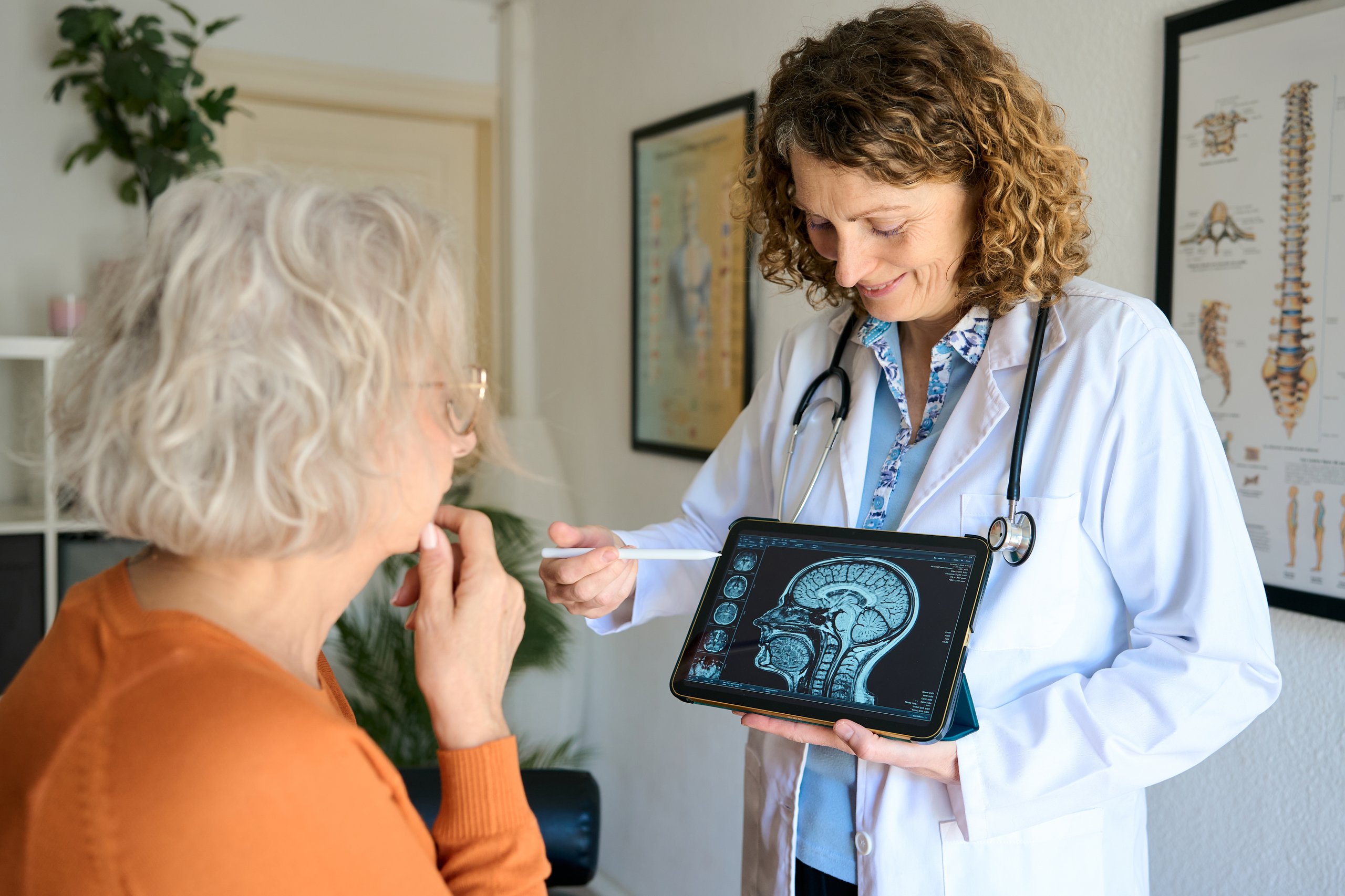 Médico explicando resultados de resonancia cerebral en tablet a paciente en consulta médica