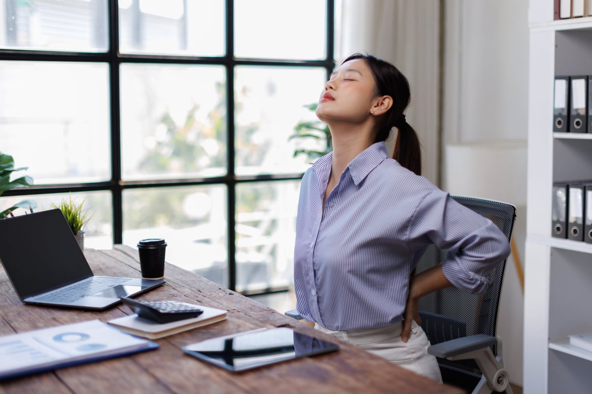 Young businesswoman stretching at a desk, relieving back and neck pain from long hours of sedentary office work