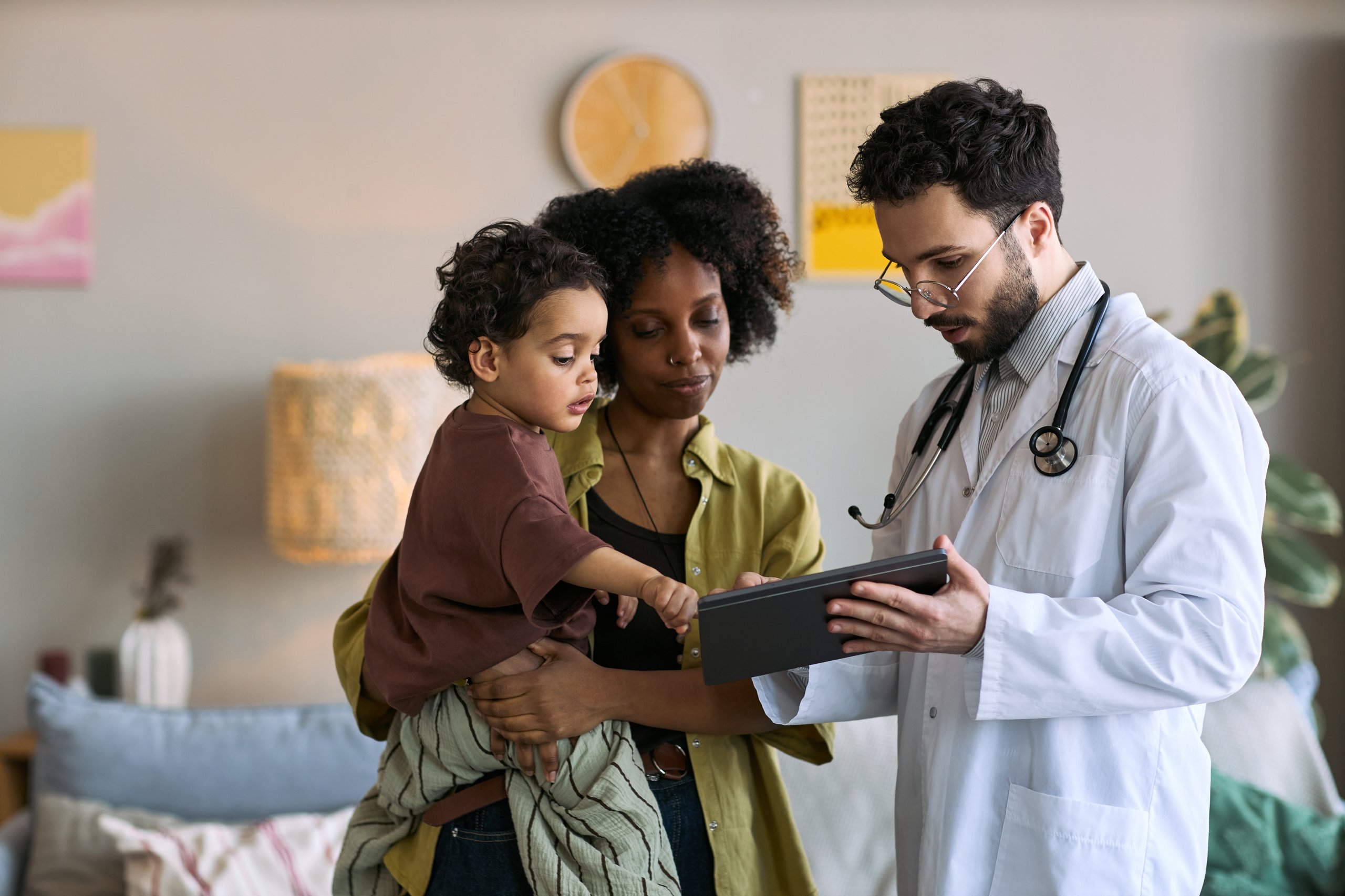 Médico mostrando tablet a madre con niño durante visita pediátrica a domicilio